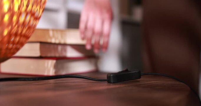 Woman turning on lamp with inline cord switch at wooden table indoors, selective focus