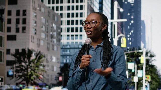 Field reporter holds microphone, speaking towards camera on city street, presenting information. African american journalist reports live news update with mic from downtown area.