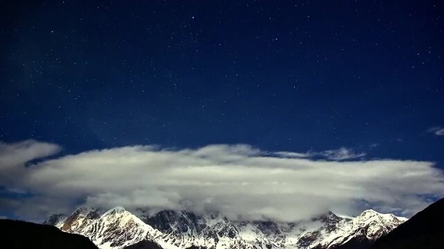 Stunning nocturnal time lapse capturing atmospheric clouds and moving stars over a majestic snowy mountain in China.