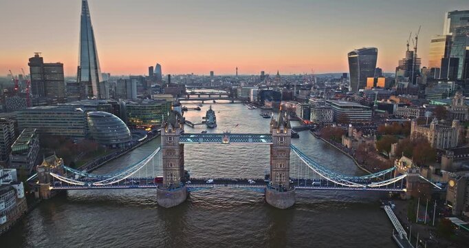 Tower Bridge crossing the Thames at sunset with The Shard and London City Hall, modern and historic skyline illuminated, reflections on the river capturing evening city life. Aerial view drone flight