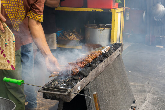 A man is grilling Sate Buntel (culinary specialty from Solo, Central Java, Indonesia), featuring minced goat or lamb meat wrap in fat and grilled over charcoal with billowing smoke. Selective focus. 