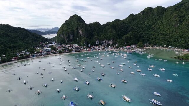 Aerial view of idyllic tropical bay with many wooden outrigger boats parked in clear turquoise water.