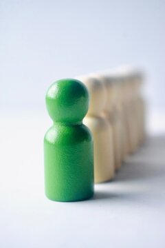 High-angle view of a green wooden figure leading a diagonal line of white figures, depicting a trailblazer and market leader.