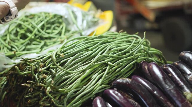 Street Vendor Arranging Yardlong Beans and Eggplants at a Roadside Stall