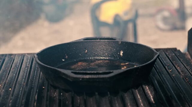 Chef using spatula to lift melted cheese topped burger patty from cast iron skillet on charcoal grill.