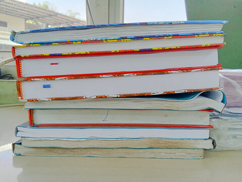 A neat stack of colorful hardcover books and notebooks on a desk