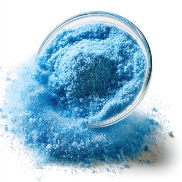 Bright blue crystalline powder spilled from a clear glass bowl on a white surface.