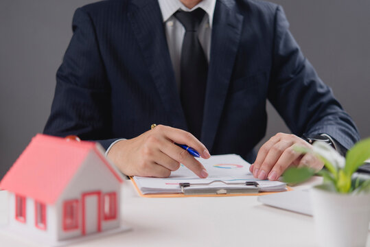 Real estate agent analyzing mortgage home loan document with house model on desk