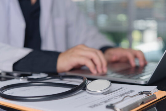 Stethoscope on insurance claim form with doctor typing laptop healthcare billing