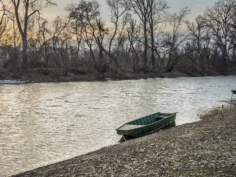 Empty rowing boat moored on the bank of the Tamis (timis) river in Glogonj, Vojvodina, Serbia, with bare riverside trees and calm winter water in the background.
