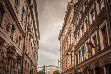 Obraz premium Narrow cobblestone street in Vecriga Vecpilseta, the Old Riga, Latvia, with historic facades, flags, street lamps and a view toward the old town architecture of the Latvian capital.