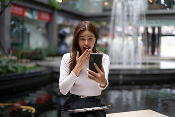 Fototapeta premium Surprised woman reacting to mobile phone content in shopping mall
