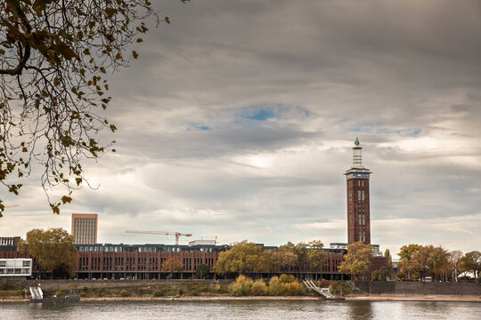 Panorama of Cologne Fair, Kolnmesse, and the Rheinhallen by the Rhine river in Cologne, Germany, with tower, autumn trees and cloudy sky.