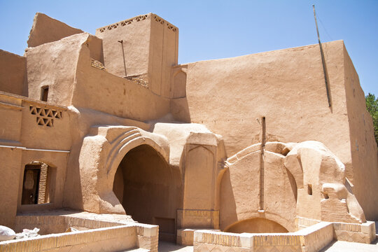 Traditional mud-brick building in the old town of Yazd, Iran, with clay walls, an arched doorway and a windcatcher tower, illustrating the distinctive desert architecture of central Iran.