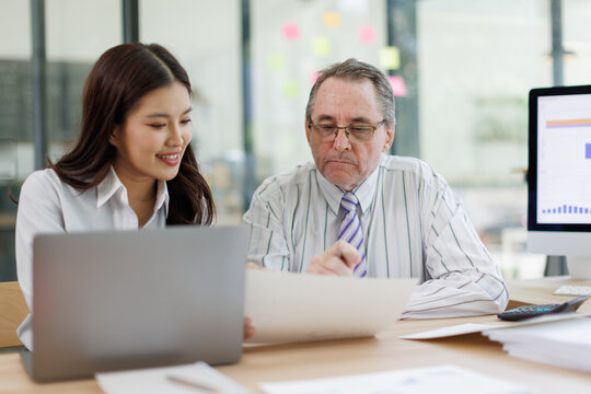 Business colleagues collaborating on a project, analyzing data in a modern office, junior worker learning from senior manager while discussing financial reports and strategy