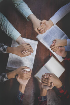 Christian group of people holding hands praying worships together to believe and Bible on a wooden table for devotional for prayer meeting concept. Christian worship and pray.  teamwork.
