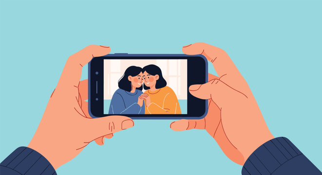 Person uses a modern smartphone to take a photograph of two happy women smiling and holding hands in a bright room.