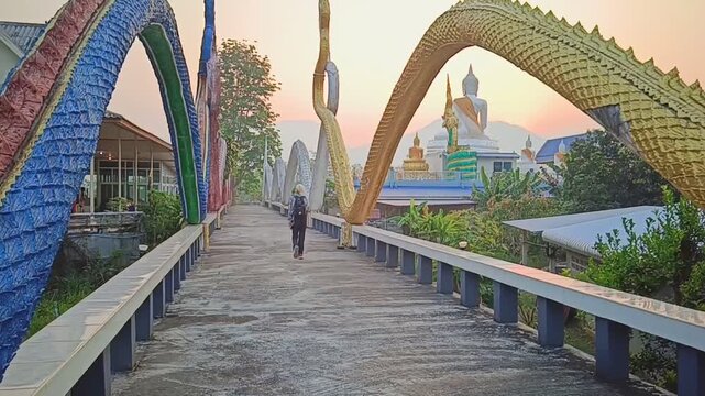 Female Tourist Walking Across a Bridge Flanked by Colorful Naga Statues at Wat Phra That Mae Yen in Pai, Thailand.