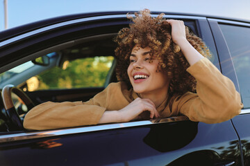 Fototapeta premium Cheerful woman leaning out of a car window, smiling with sunlit hair, outdoor vibe, casual lifestyle moment, retro film color tones, bright natural hues, candid travel mood