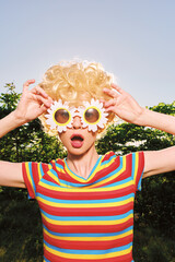 Fototapeta premium Smiling woman with curly blonde hair wearing a striped colorful shirt outdoors on a sunny day, playful retro vibe with flower glasses and vibrant mood.