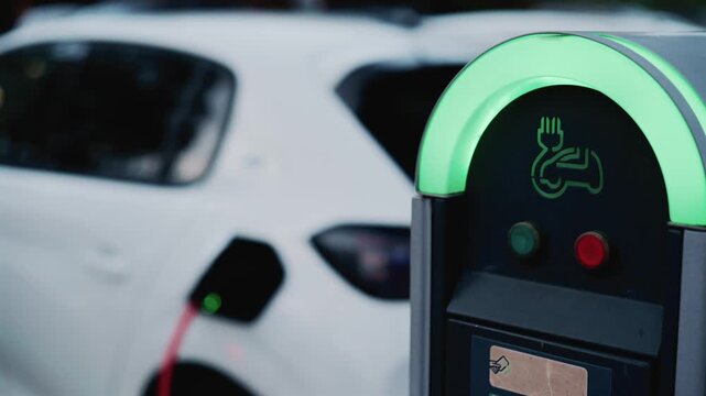 Electric vehicle charging station with green status indicator light outdoors.