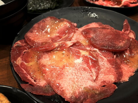 A close-up image of thinly sliced, raw beef tongue marinated in sauce, ready for Japanese yakiniku grilling.