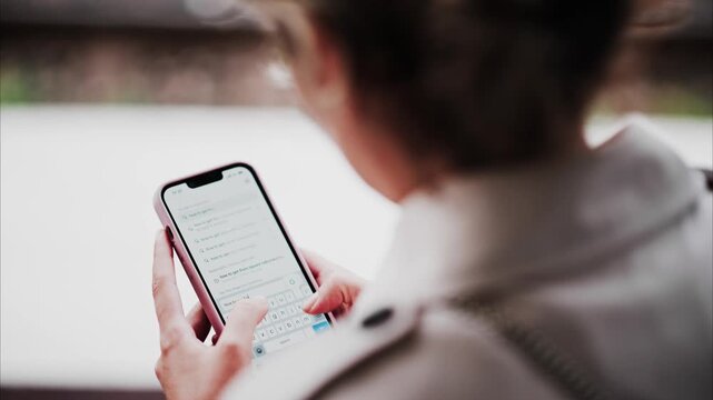 Woman typing search query on smartphone screen while standing outdoors.