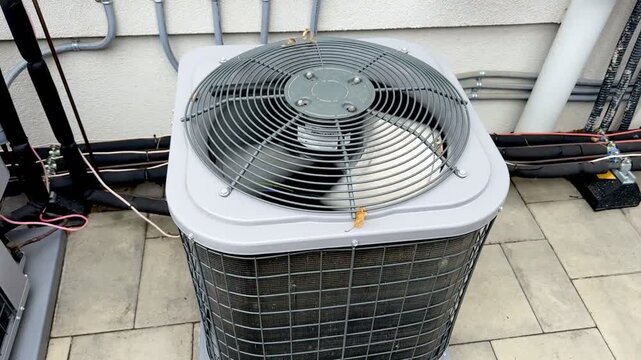 Outdoor HVAC air conditioner unit fan.iew of an outdoor air conditioning condenser unit with protective metal grille and rotating fan,