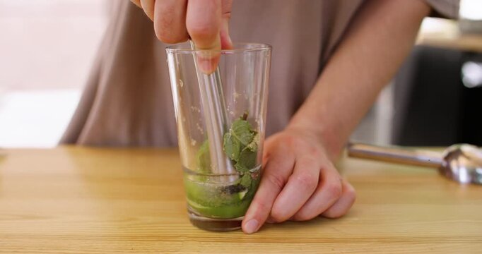 Beverage mojito ingredient. Cocktail preparing. Unrecognizable bartender hand mixing fresh mint leaves lime wedges in glass for classic drink in bar.