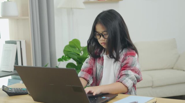 Young girl working on a laptop in a modern living room, wearing glasses and a plaid shirt, focused on her online activities, with houseplants and books in the background