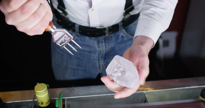 Ice cube split. Beverage preparing. Unrecognizable male bartender hands using professional frost crushing metal tool at workplace.