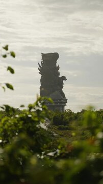 Distant view of the monumental Garuda Wisnu Kencana statue rising above tropical foliage in Bali, Indonesia.