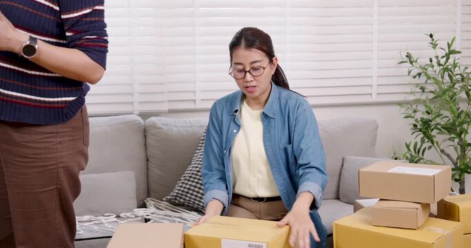 Asian female entrepreneur sealing parcel box with tape, preparing package for delivery, managing online shopping parcel box process during daily home based e-commerce business workflow