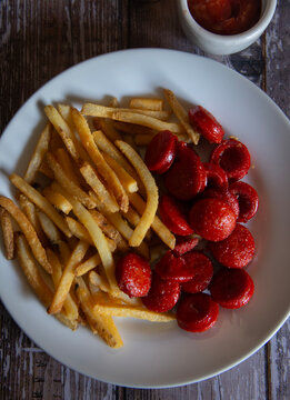 french frries and bubbas and a small bowl of ketchup, snack, beer over a rustic wooden table. Chilli Beans Fries and Bubbas. cenital or close up top view.