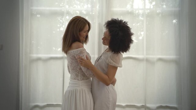 Lesbian couple sharing a romantic moment together in front of a bright window during a same sex wedding celebration at home