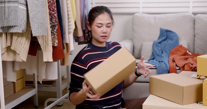 Asian woman small business owner lifting parcel box, rotating package slowly, checking shipping detail, preparing online shopping parcel box during slow motion e-commerce packing workflow at home