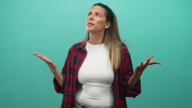 Woman in red plaid shirt raises palms in a shrugging gesture with expressive face in studio; exasperation doubt.
