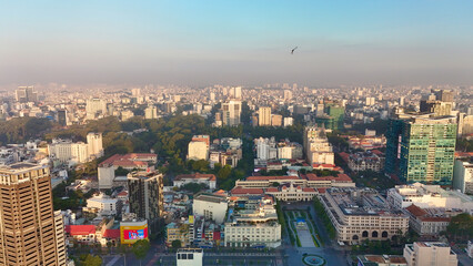 Fototapeta premium Ho Chi Minh City, Vietnam – 4K aerial sunrise drone view of downtown skyline with modern skyscrapers, dense urban housing, busy streets and morning traffic along the Saigon River in Southeast Asia