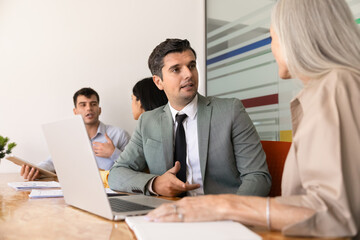 Obraz premium Businessman speaking with woman colleague at conference table, discussing ideas, explaining strategy, consulting corporate client during professional office meeting. Communication, teamwork, business