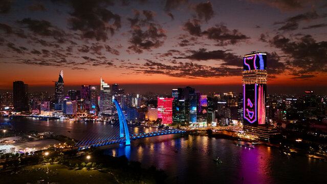 Ho Chi Minh City, Vietnam: 4K Aerial Night Drone View of Skyline, Skyscrapers, Towers, Saigon River, illuminated Bason Bridge and Streets, Busy Traffic in Evening