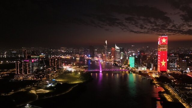 Ho Chi Minh City, Vietnam: 4K Aerial Night Drone View of Skyline, Skyscrapers, Towers, Saigon River, illuminated Bason Bridge and Streets, Busy Traffic in Evening