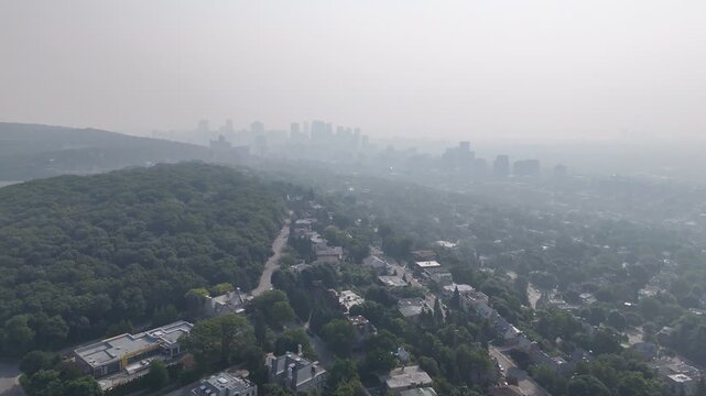Hazy aerial view of Westmount and downtown Montreal skyline hidden behind smog and trees. c.