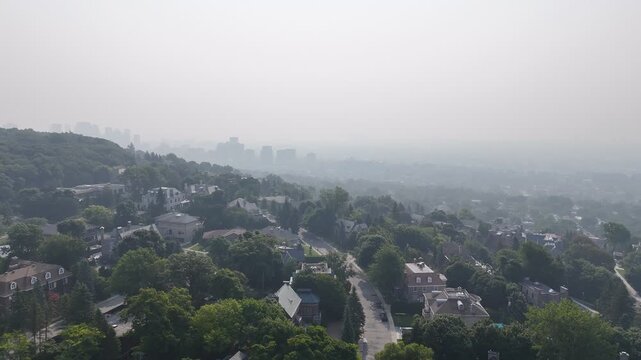 Hazy aerial view of Westmount and downtown Montreal skyline hidden behind smog and trees. c.