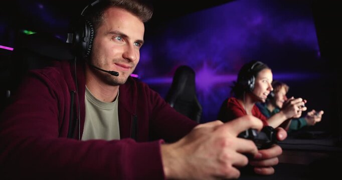 Group of friends, gamers wear headsets playing video games together in gaming club, interacting during multiplayer session, holding controllers, enjoying competitive entertainment in esports cybercafe