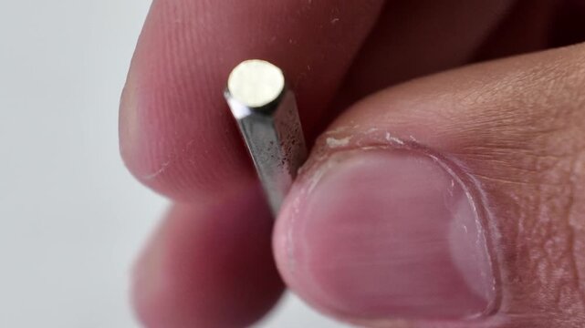 Macro view of a human hand picking up a heavy socket hex nut driver bit tool from a gray textured backdrop surface.