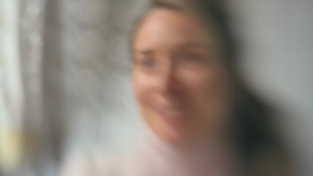 Blurred portrait of woman looking towards camera during soft focus indoor conversation.