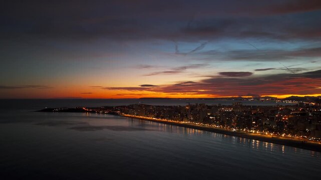 Illuminated city of Alicante, beach during dramatic and colorful sunrise over Mediterranean Sea in Spain. Aerial drone, copy space