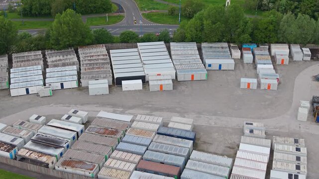 Sideways Aerial of Stored Shipping Containers in Industrial Depot. Organized stacks of steel cargo. Surplus inventory, logistics management, massive scale of industrial storage solutions. UK.