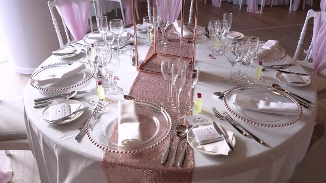 A beautifully arranged round table displays glasses, cutlery, and napkins ready for a gathering. The table is set with a light-colored cloth and decorative elements for a special occasion.