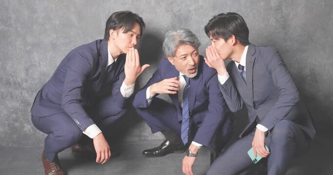 座り込んで噂話をするスーツ姿のビジネスマン3人